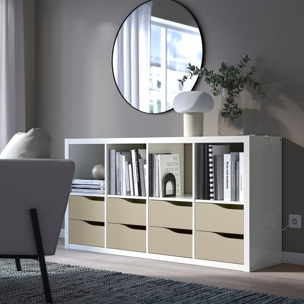 White KALLAX storage unit with drawers and shelves; large, holds books, decor, next to a grey chair.