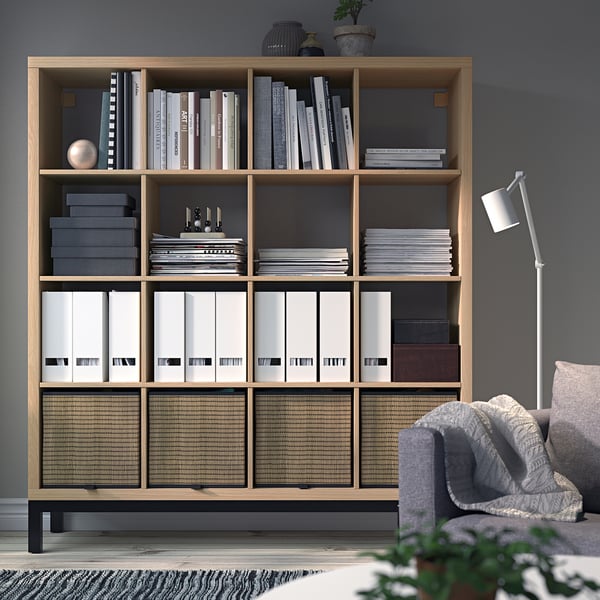 KALLAX shelf with books, files, decor. Tall, next to grey chair, dark grey walls.