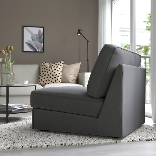 Modern living room with grey KIVIK sofa-bed, designed for small spaces. Large window lets in natural light. Decorative pillows and flowers add style.