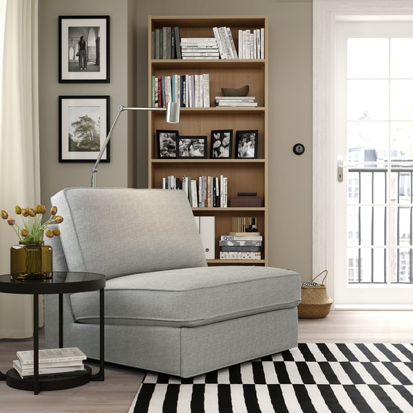 Modern living room with KIVIK sofa, striped rug, bookshelf, side table & large window.