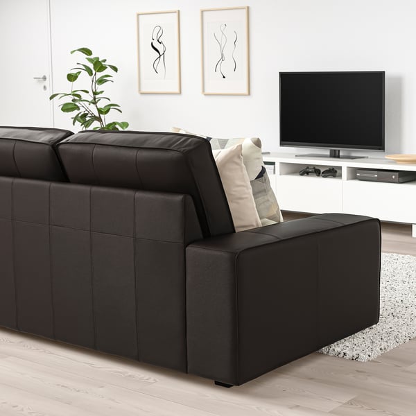 Modern living room with large KIVIK black leather sofa, geometric throw pillows, flat screen tv, and abstract wall art.
