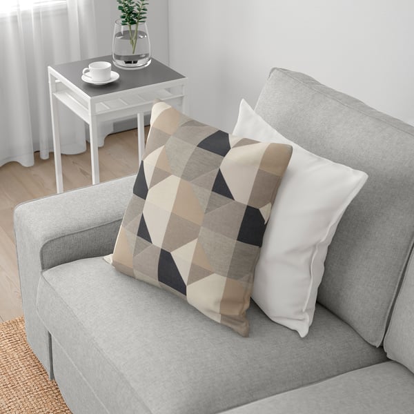Grey sofa with chequered and white pillows, wooden side table with tea set and plant.