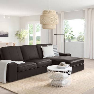 Modern living room with large black KIVIK sofa, white coffee table, hanging lamp, and large window with curtains.