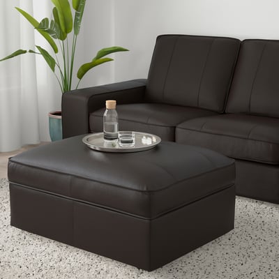 Modern living room with KIVIK black leather sofa and ottoman; ottoman has a tray with a bottle and glass, plant nearby.