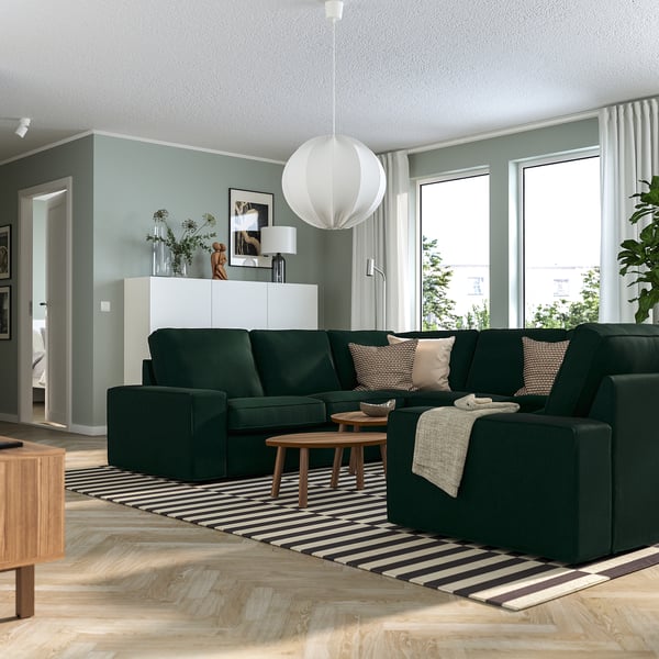Modern living room with green KIVIK sofa, striped rug, coffee table, pendant light, large windows, blue walls, white cabinet, and decor.