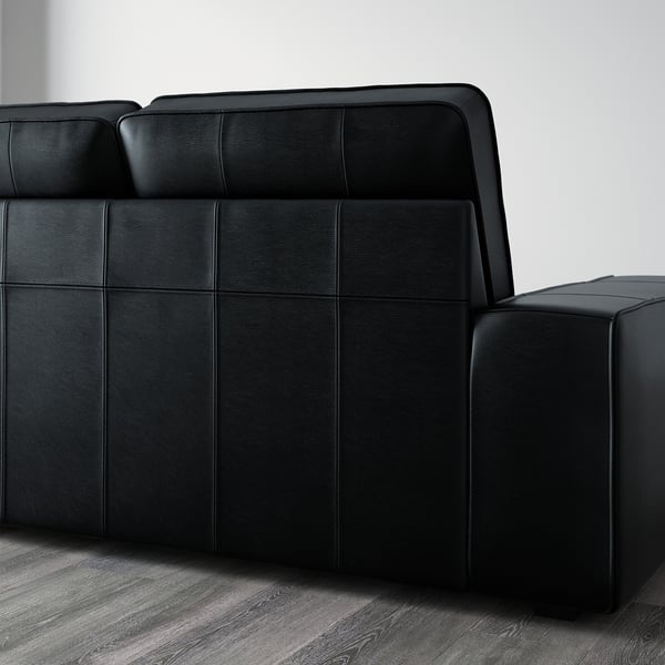 Black KIVIK sofa with padded armrests on wooden floor. Deep seat cushions for comfort.
