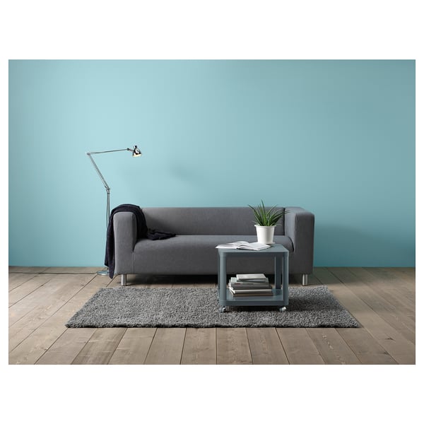 Modern grey sofa against blue wall, with throw blanket, plant, books, and lamp.