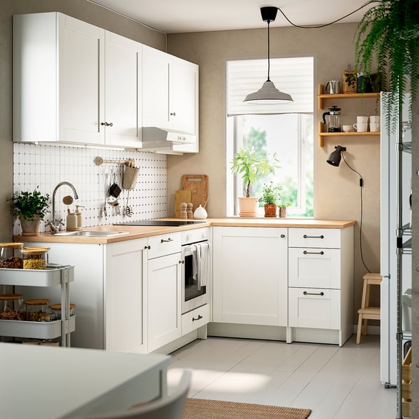 Small, white, l-shaped kitchen with oak countertop, plants, and hanging light.