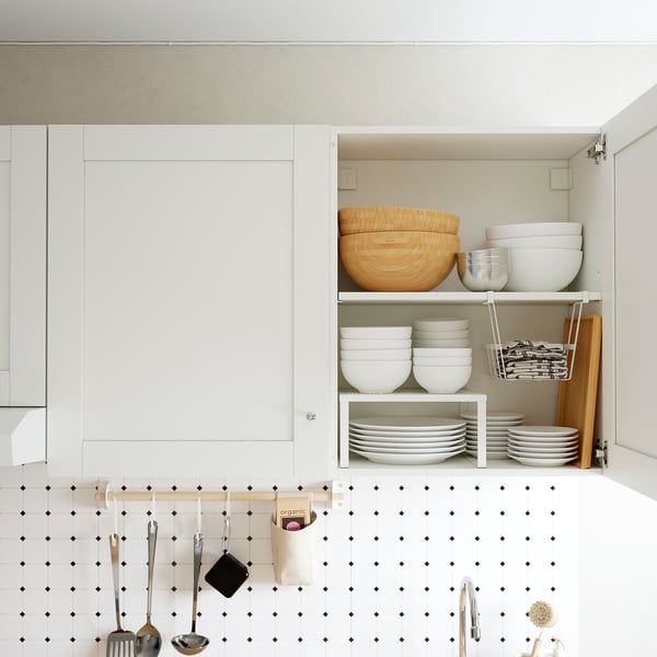 Kitchen cabinet open, displaying organised bowls, plates, and utensils; showing practical storage and easy access.
