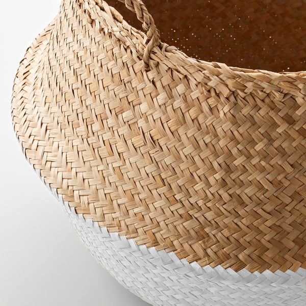 Handwoven seagrass basket with sturdy handles, partially dipped in white, resting on a brown surface.