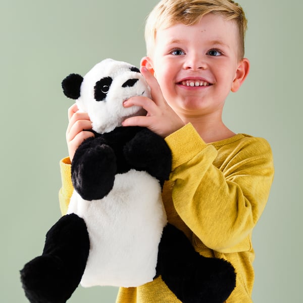 A young boy, wearing a yellow shirt, smiles while holding a black and white stuffed panda toy.
