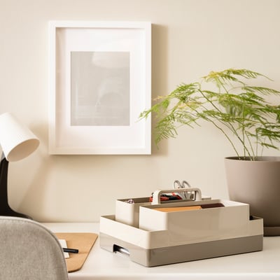 Desk with KUGGIS white organiser, plant, lamp, and framed art. Organiser fits under frame, next to plant.