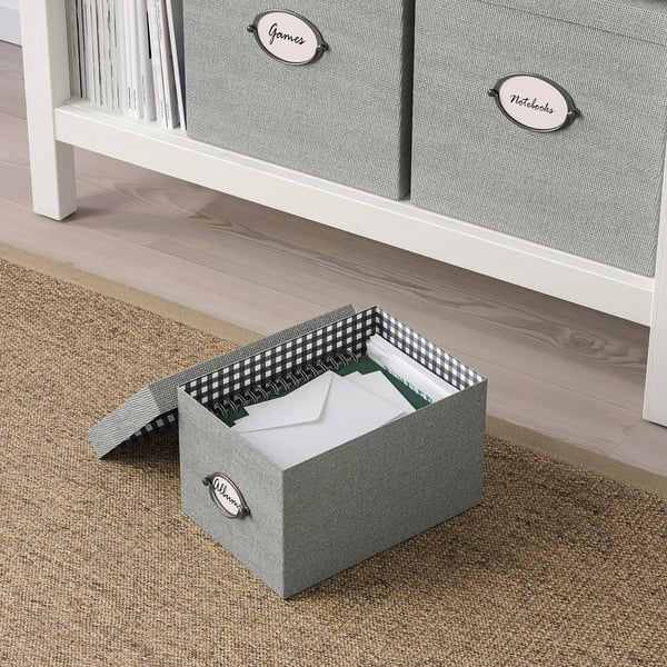 Three labelled fabric storage boxes - open one shows folders, near wooden floor and shelf.