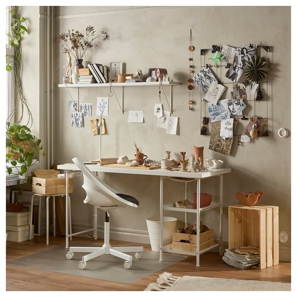 White workspace with table, chair, storage, art supplies, posters.