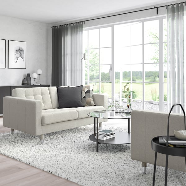 Modern living room: white sofa, glass table, speckled rug, windows with views, minimalist decor.
