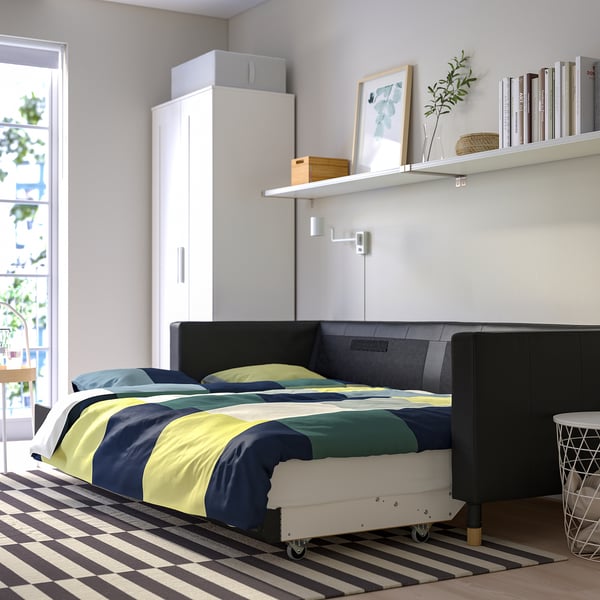 Modern bedroom with LANDSKRONA sofa-bed featuring thick leather and fabric upholstery, storage space, and a bookshelf with decorative items.