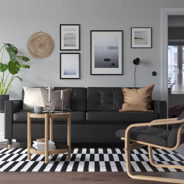 Black leather sofa with cushions and coffee table, chequered rug, wall art, cosy ambiance.