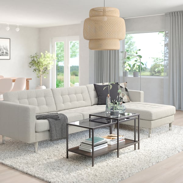 Modern living room with white l-shaped LANDSKRONA sofa, grey throw, glass coffee table, and large window. Stylish, minimalist decor.