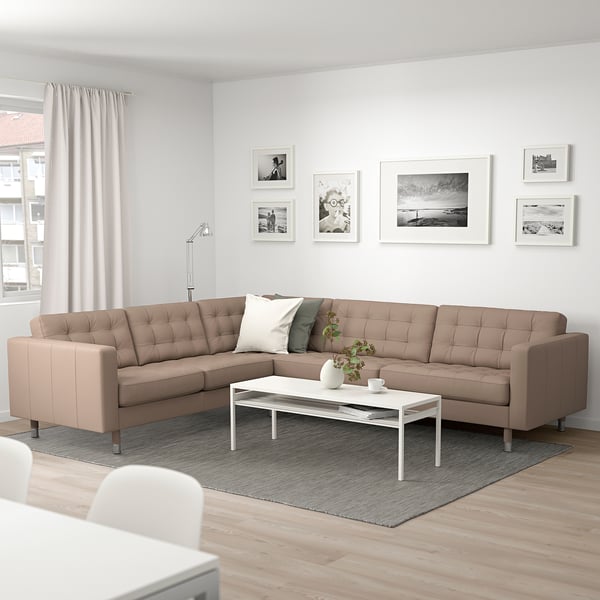 Modern living room with beige l-shaped sofa, white coffee table, grey rug, floor lamp, and black/white wall art.