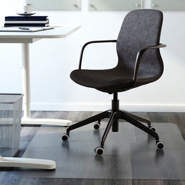 Modern black office chair with armrests and wheels under a white desk on a glass mat.