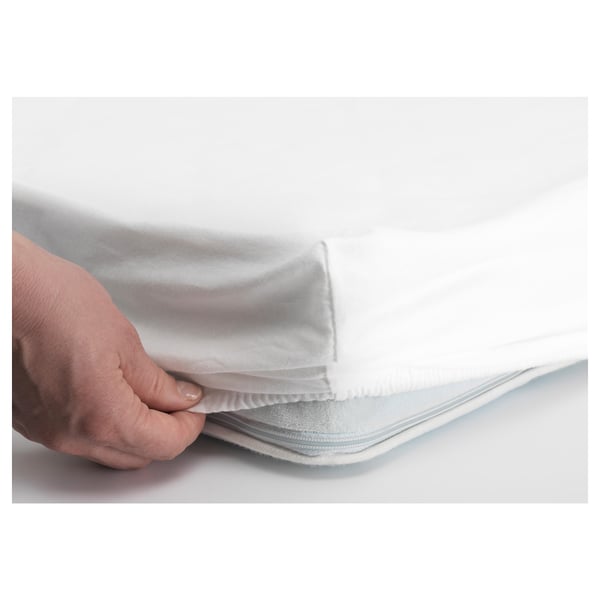 Hand holding an elastic edge of a white fitted sheet, demonstrating how it secures to a mattress.