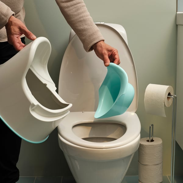 Person pouring water from white pitcher into white toilet with blue insert, green wall, toilet paper roll.