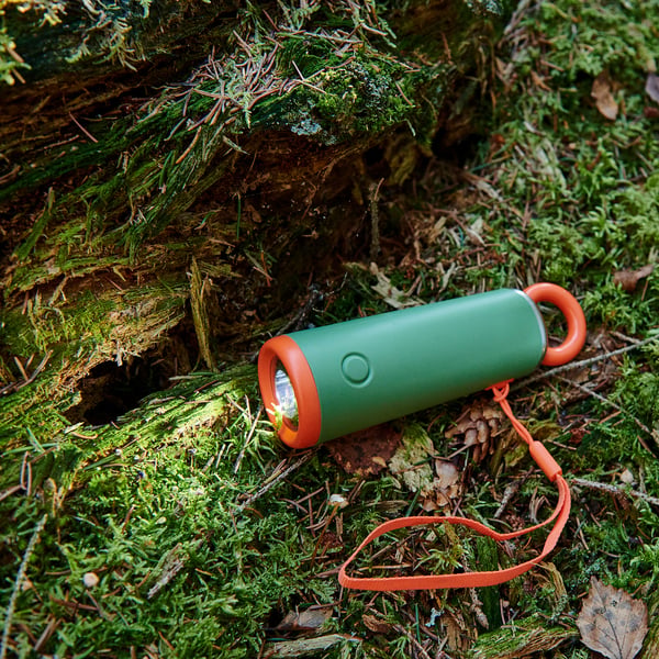 Green torch with orange accents and lanyard, resting on mossy forest floor. Quality materials for durability.