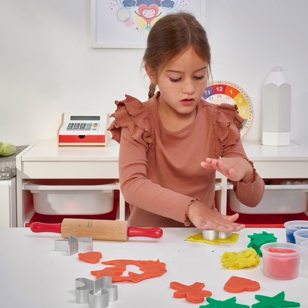 A young girl plays with MÅLA modelling dough, cutting shapes with included cutters, using a rolling pin.