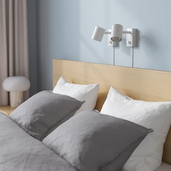 Blue bedroom with a wooden headboard bed featuring grey and white bedding. Two wall-mounted lights above the bed.