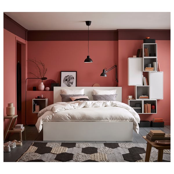 Modern bedroom with pink walls, white MALM bed, geometric rug, shelving unit, pendant lamp, and decorative items.