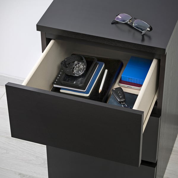 Open black drawer of MALM chest, holding watch, books, keys, and box.