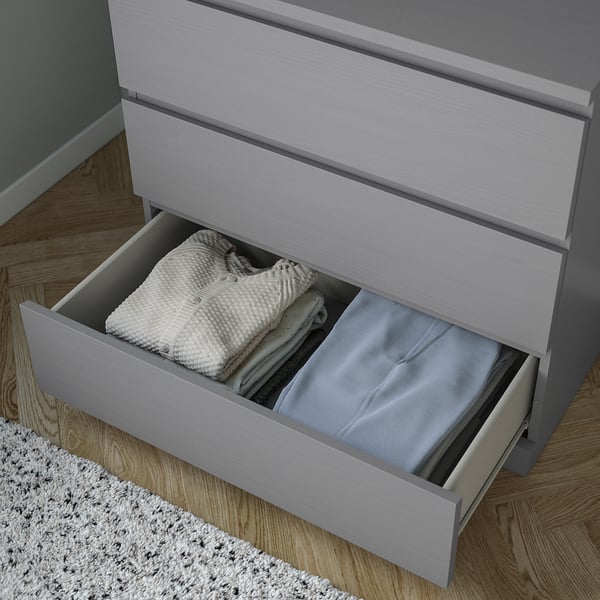 Open grey dresser shows folded clothes and linens in one drawer, smooth and safe drawers.