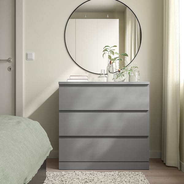 Grey MALM dresser with 3 drawers and thin legs, under black round mirror.