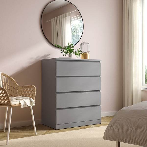 Modern bedroom with grey MALM chest, mirror, plant, and wicker chair.