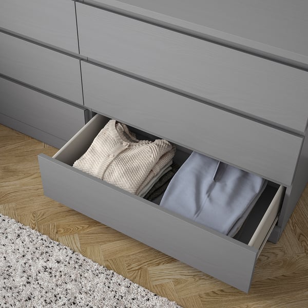 Open grey MALM chest drawer with folded clothes on wood floor.