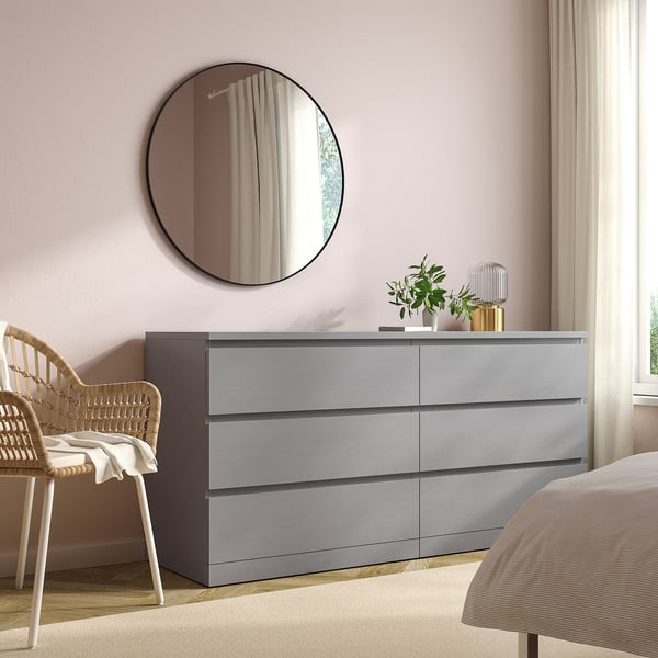 Modern bedroom with a grey MALM dresser, wicker chair, and circular mirror.