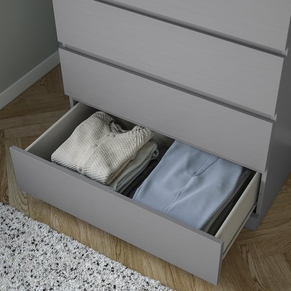 Open grey chest of drawers with folded clothes inside. Drawers have smooth runners and safety stop.