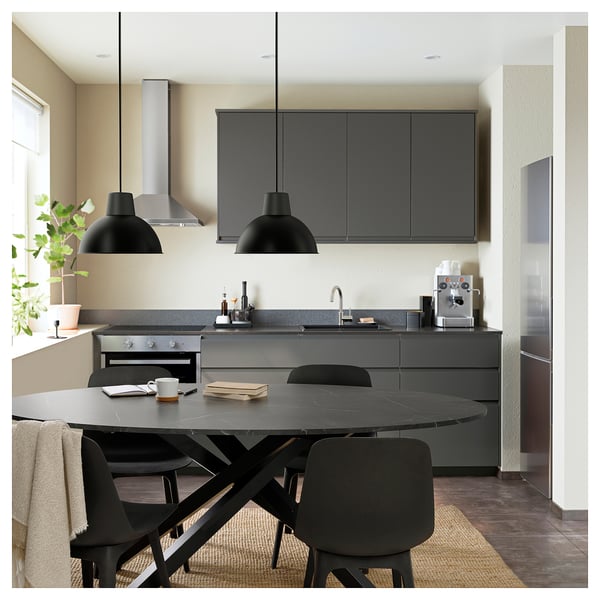 Modern kitchen with black MARIEDAMM oval table, chairs, and dark cabinets. Two black pendants, stone countertop, stainless appliances, and cream wall.