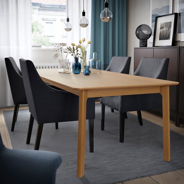 Oak dining table with grey chairs, blue rug, and flowers in vases.