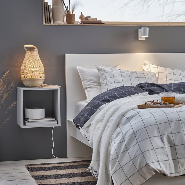 Cosy bedroom with white grid bedding, dark grey walls, wall-mounted grey MISTERHULT lamp with woven bamboo shade.