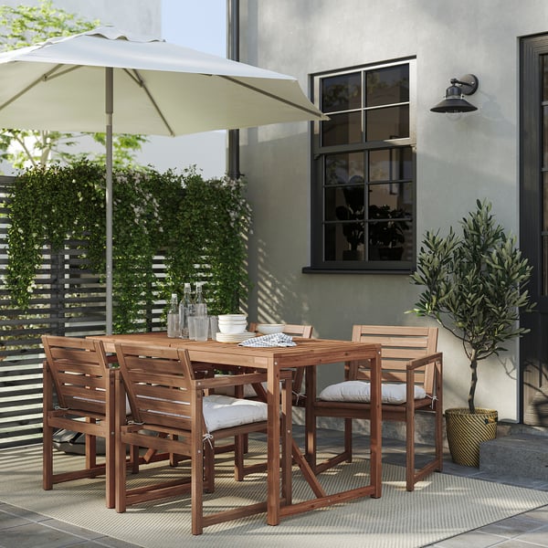 Outdoor dining set with 4 chairs, wooden table, and cream cushions under white umbrella.
