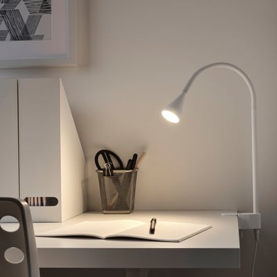 Silver NÄVLINGE lamp clamped on desk with pen holder and book.