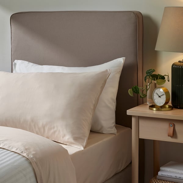 Modern bedroom with NATTJASMIN silk pillowcases, gold clock, green plant, & beige lamp on nightstand.