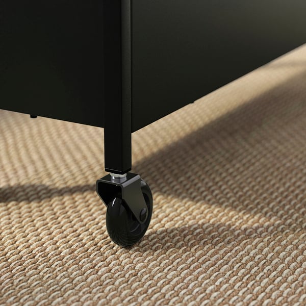 Black metal trolley wheel, robust and sturdy, mounted on a woven beige rug.