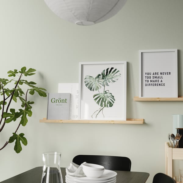 A modern dining room a wooden shelf displaying framed art, books, and a plant. A table set with cups and plates is set below.