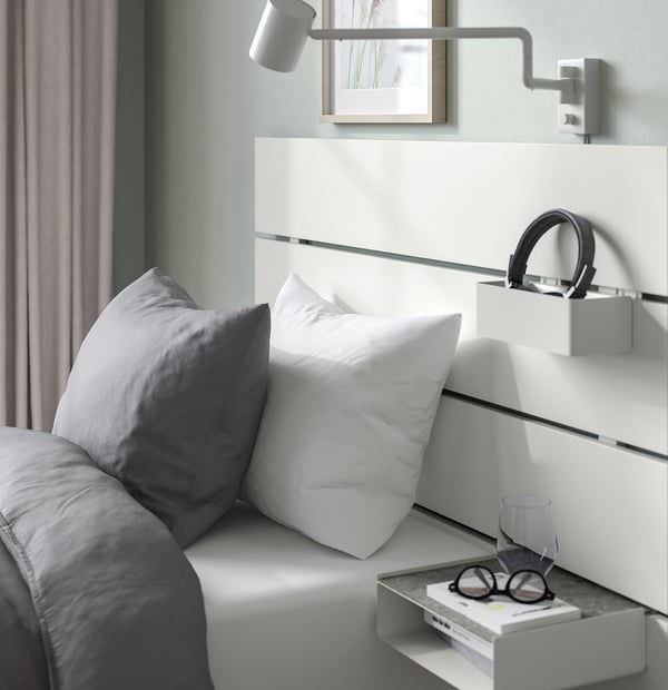 Modern bedroom with NORDLI bed, drawers, shelf headboard, wall lamp, grey and white bedding.