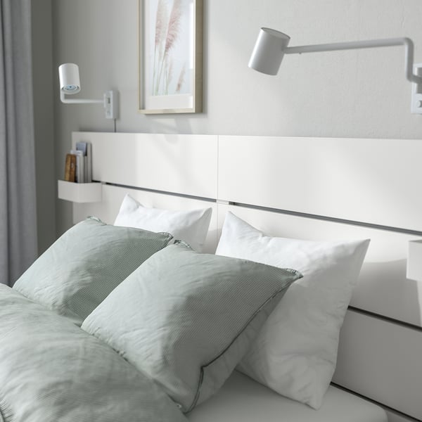 Minimalist bedroom setup with white bed, light green bedding, wall-mounted lamps, and headboard shelves.