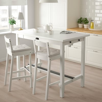 White bar stool with curved back, cushioned seat, and solid wood frame next to matching table in kitchen.