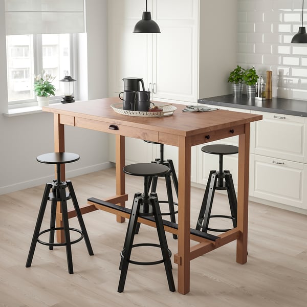 A NORDVIKEN kitchen table and chairs. Light brown top, dark legs, black seats. Offers dining space, storage in drawer and hooks. Modern, minimalist.