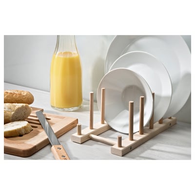 Wooden dish rack with dowels holding white plates. Orange juice and bread nearby.